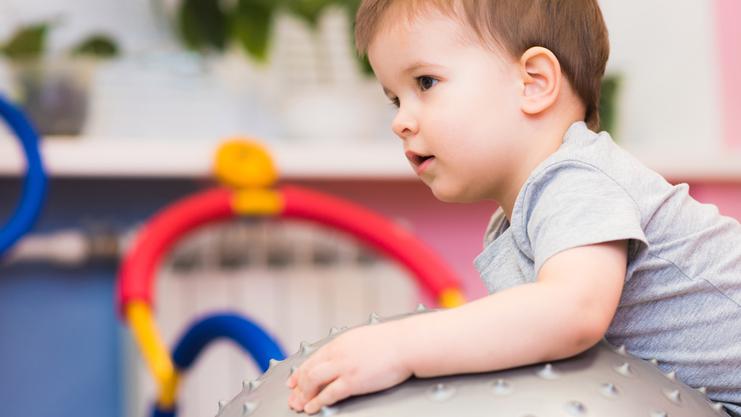 Kleines Kind sitzt auf einem großen, stacheligen Gymnastikball in einem bunten Spielzimmer.