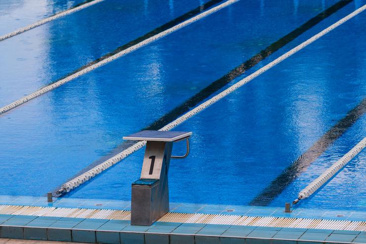 Startblock mit der Nummer 1 am Beckenrand eines Schwimmbeckens mit blauen Wasserbahnen im Hintergrund.